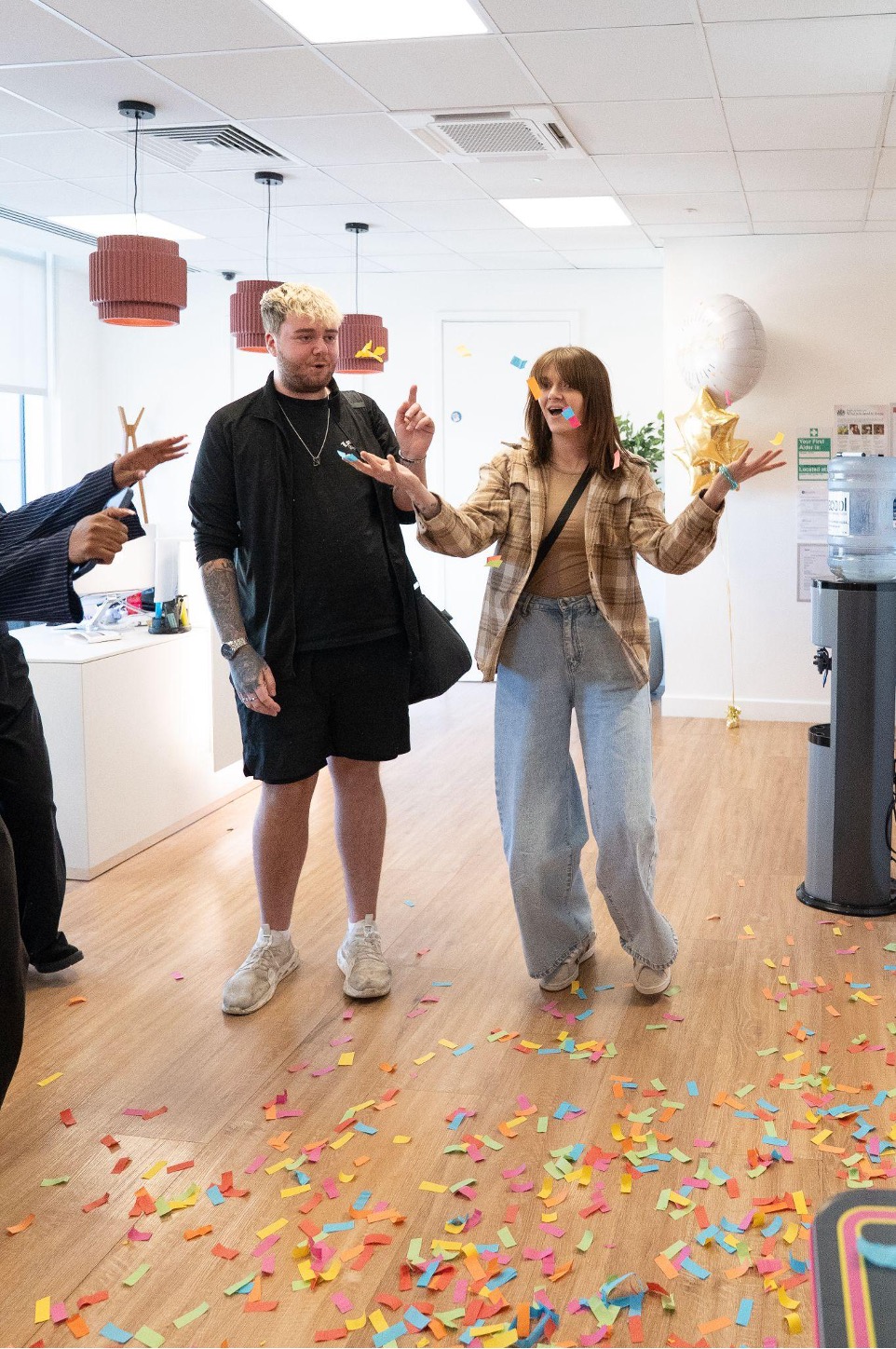 Liam walking into an office through falling confetti as Chaotic staff applaud, celebrating a £10,000 competition win
