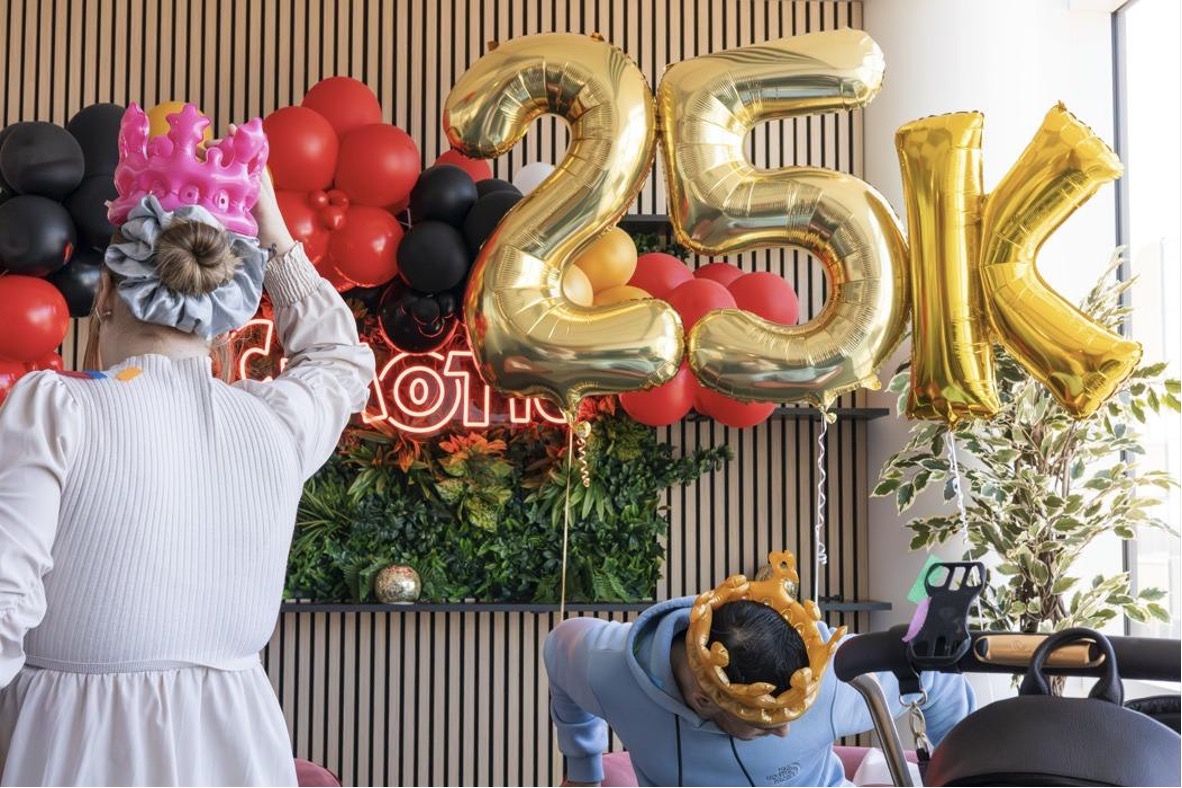 Celebration scene at Chaotic HQ with gold “25K” balloons, confetti, and people wearing crowns