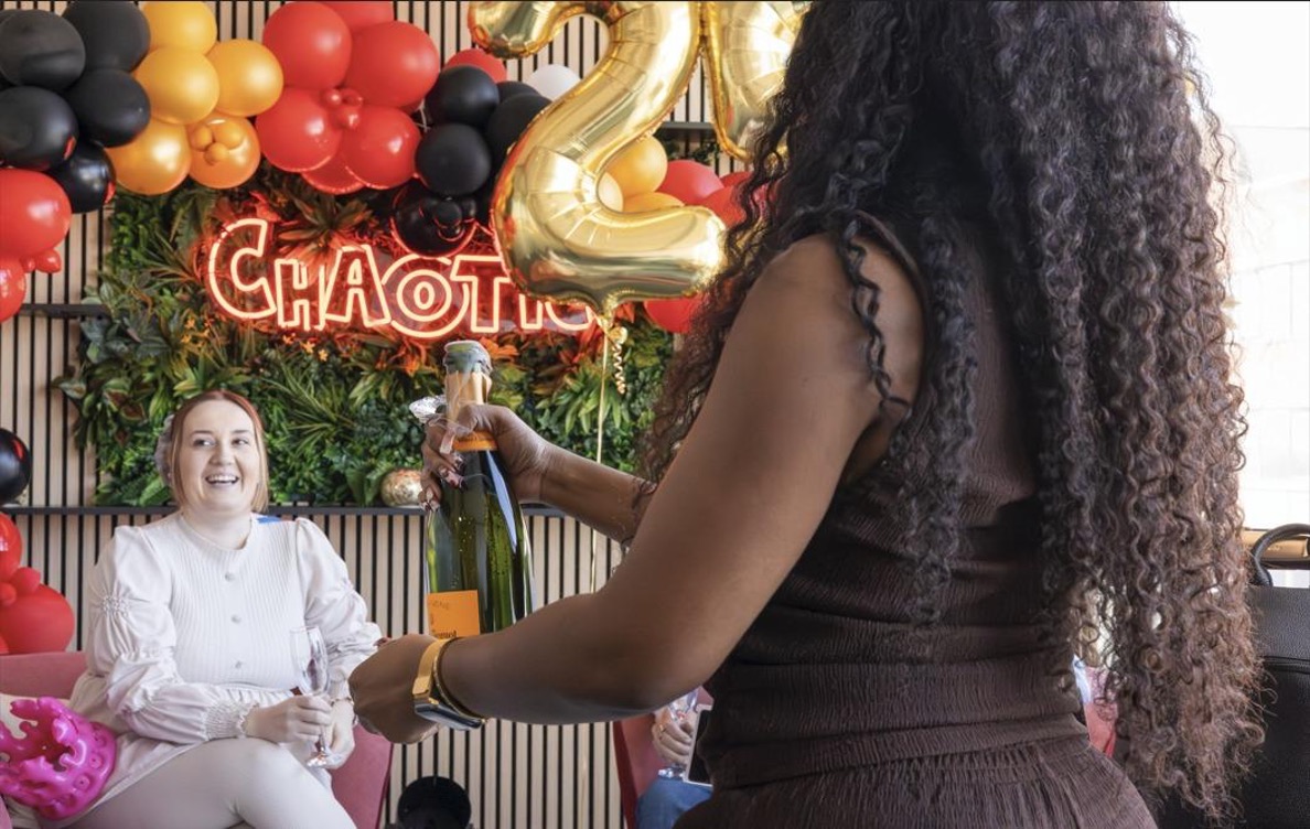 Shantel presenting a bottle of champagne during a £25,000 winner celebration at Chaotic HQ with “CHAOTIC” sign and gold balloons in the background