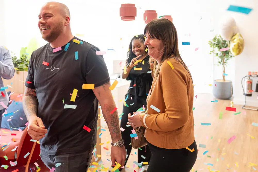 Josh walking into an office through falling confetti as Chaotic staff applaud, celebrating a £10,000 competition win